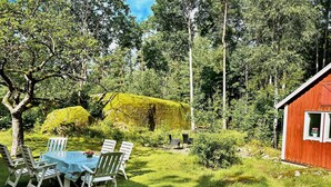 Un cadre extérieur rustique avec une table et des chaises en bois, entouré d’une végétation luxuriante et d’une petite cabane rouge.