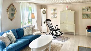 Un salon avec un canapé bleu, une table basse blanche, un fauteuil à bascule noir, un meuble blanc et des tableaux encadrés accrochés au mur.