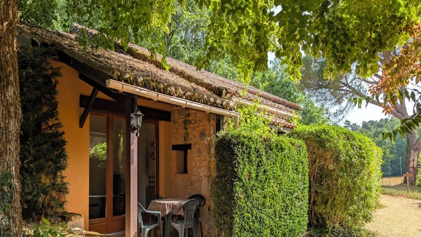 A rustic building with a stone wall, a wooden door, and a table with chairs outside. - Charming little cottage in an exceptional Holiday Resort **** in Dordogne-Lot (Gavaudun)