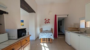 A kitchen with a microwave, wooden cabinets, a dining table with chairs, and a red curtain. - Charming little cottage in an exceptional Holiday Resort **** in Dordogne-Lot (Gavaudun)