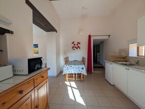 A kitchen with a microwave, wooden cabinets, a dining table with chairs, and a red curtain. - Charming little cottage in an exceptional Holiday Resort **** in Dordogne-Lot (Gavaudun)