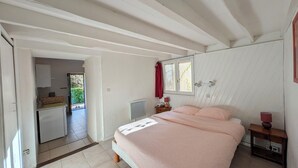 A bedroom with a bed, a bedside table, a window, and a view of a kitchen and outdoor area. - Charming little cottage in an exceptional Holiday Resort **** in Dordogne-Lot (Gavaudun)