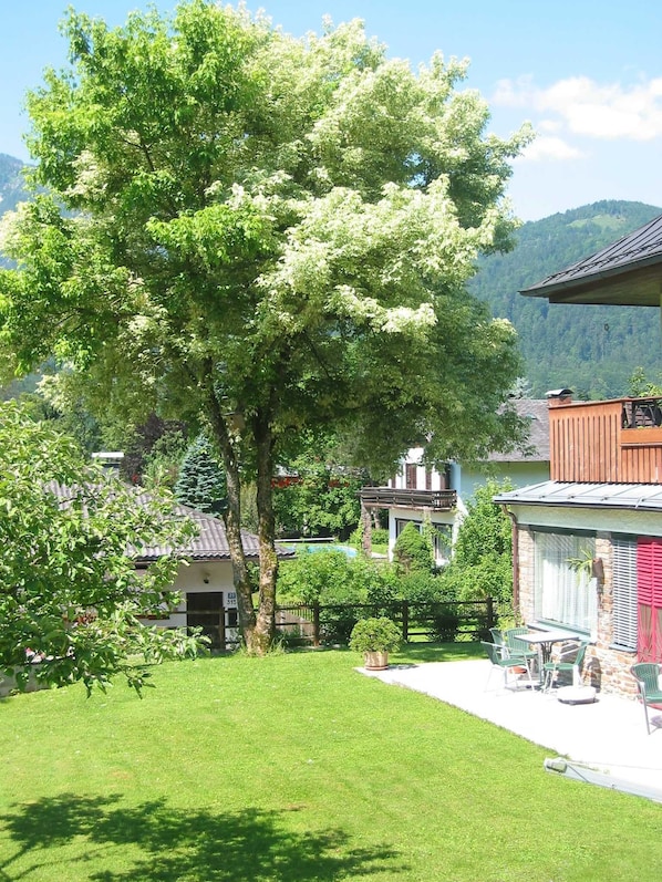 A residential area with a large tree, a house with a balcony, and a clear view of the surrounding landscape.
