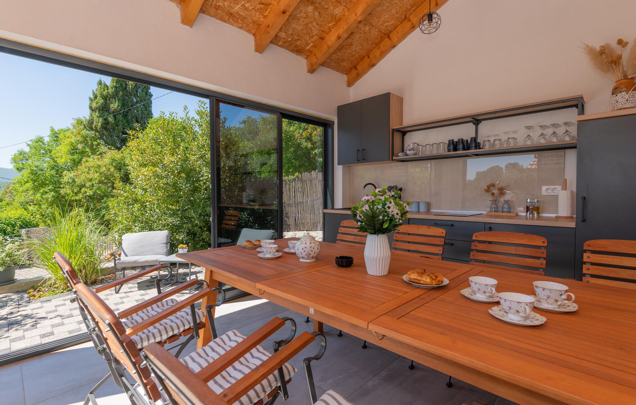 A modern dining area with a wooden table, chairs, and a large window offering a view of greenery and trees.
