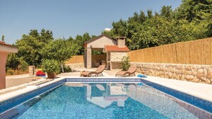 En swimmingpool med liggestole, en bygning i sten og et træhegn.