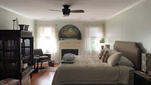 A bedroom with a bed, a fireplace, a ceiling fan, and a bookshelf.