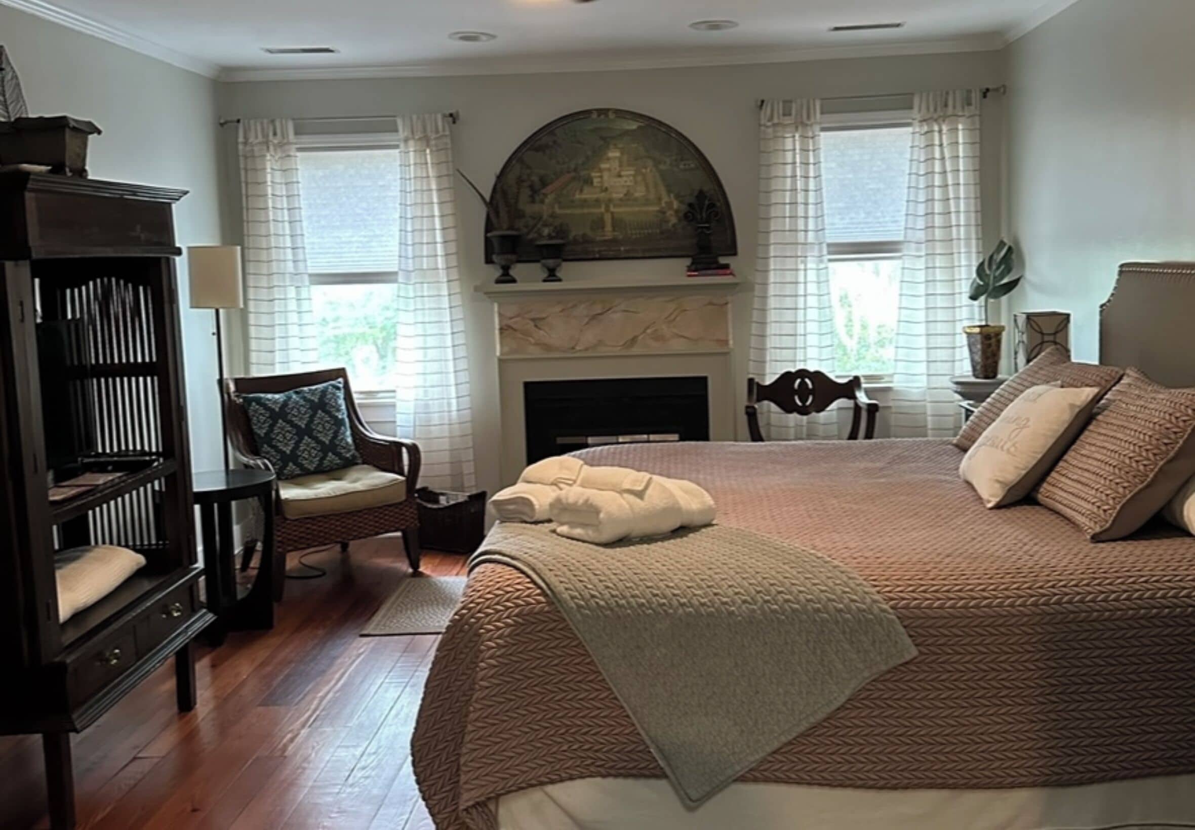 A bedroom with a large bed, a fireplace, a bookshelf, and a chair.