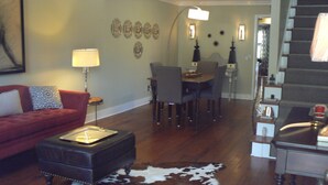 A living room with a red sofa, a coffee table, a dining table with chairs, and a cowhide rug.