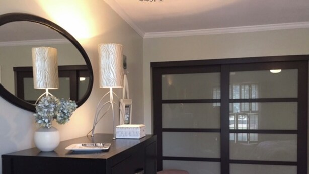 A bedroom with a dark dresser, a round mirror, two lamps, a small chair, and a sliding glass door.