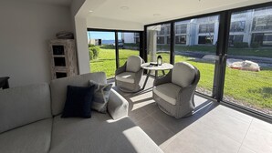 A modern living room with a large glass door leading to a balcony, a sofa, two wicker chairs, and a small table.