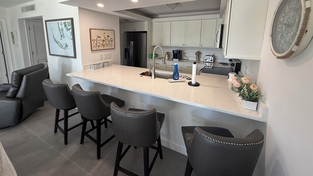 A modern kitchen with a central island, bar stools, a refrigerator, and a coffee maker.