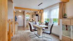 A modern kitchen with wooden beams, a dining table with chairs, and a view of the garden through large windows. - Apartment A - Holiday home Teuber (Trassenheide)