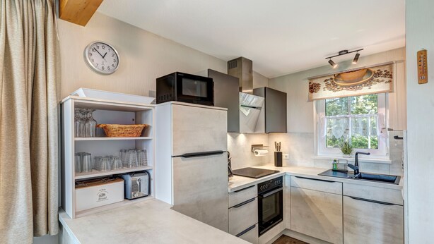 A modern kitchen with built-in appliances, a clock, and a window with a view. - Apartment A - Holiday home Teuber (Trassenheide)