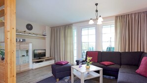 A modern living room with a sofa, ottoman, coffee table, TV, and a wooden cabinet. - Apartment A - Holiday home Teuber (Trassenheide)