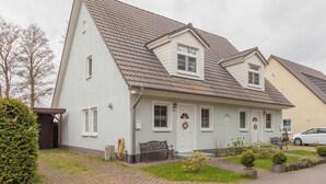 A two-story house with a sloped roof, a front porch, and a small garden. - Apartment A - Holiday home Teuber (Trassenheide)