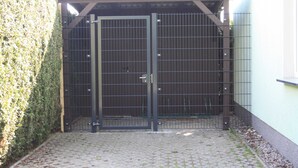A gated entrance with a metal gate, a paved pathway, and a hedge. - Apartment A - Holiday home Teuber (Trassenheide)