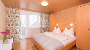 A bedroom with a wooden bed, white pillows, a bedside table with a vase of flowers, and a wooden wardrobe. - Apartment Bleckwand - Apartment house Roland (Strobl)