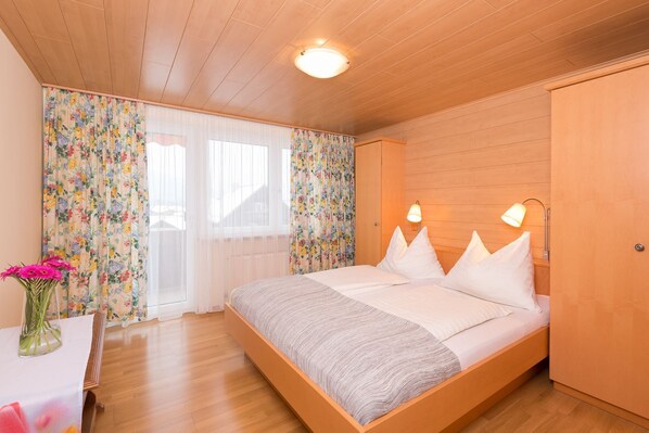 A bedroom with a wooden bed, two bedside lamps, and a window with floral curtains.
