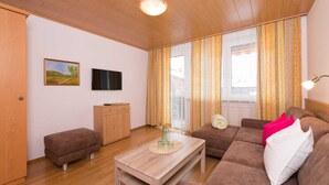 A living room with a wooden ceiling, a television on the wall, a sofa, a coffee table, and a window with curtains. - Apartment Bleckwand - Apartment house Roland (Strobl)