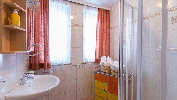 A bathroom with a sink, mirror, and a glass shower enclosure. - Apartment Bleckwand - Apartment house Roland (Strobl)