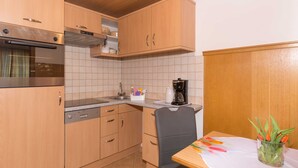 A kitchen with wooden cabinets, a dishwasher, a stove, a coffee maker, and a table with a vase of flowers. - Apartment Bleckwand - Apartment house Roland (Strobl)