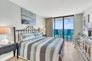 Quarto de hotel com uma cama grande, escrivaninha, cadeira, televisão e varanda com vista para o oceano.