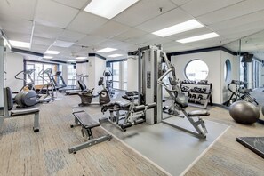 Un gimnasio con diversos equipos de ejercicio, ventanas amplias y un espejo grande.