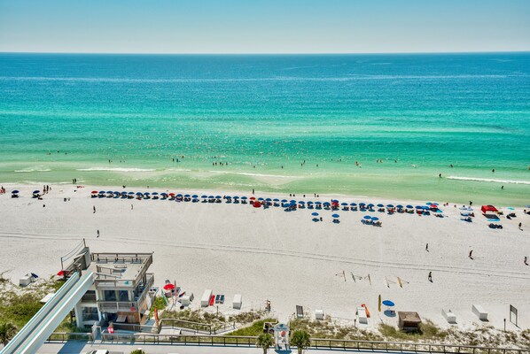 A beach with umbrellas and beach chairs, a lifeguard tower, and a clear view of the ocean.