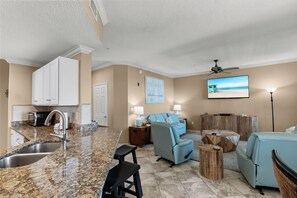 A modern living room with a kitchen area, a flat-screen TV, and a ceiling fan.