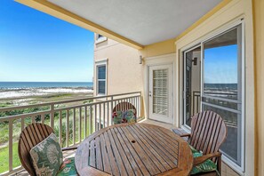 Ein Balkon mit Blick auf den Strand, ein runder Holztisch und zwei Holzstühle mit Kissen.