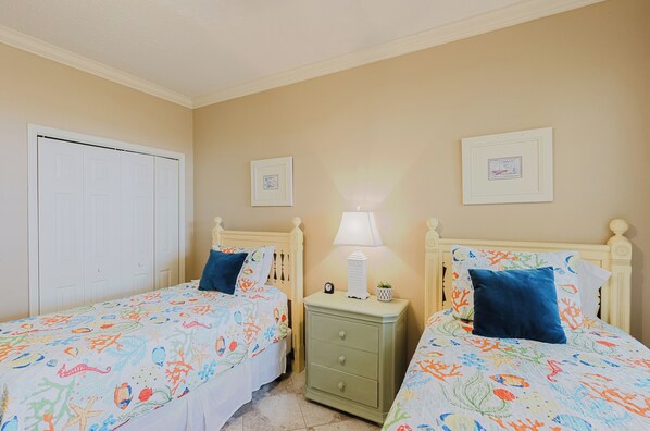 A bedroom with two beds, a nightstand with a lamp, and two framed pictures on the wall.