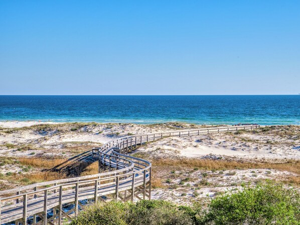 A wooden boardwalk leading to a beach with clear blue water.