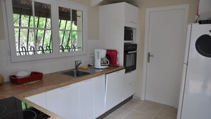 Una cocina compacta con armarios blancos, microondas integrado, horno, fregadero y cafetera.