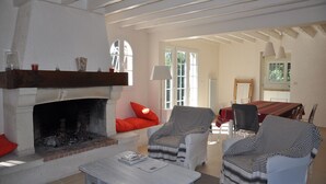 Una sala de estar con chimenea, dos sillones, una mesa de comedor con sillas y vistas al exterior a través de amplios ventanales.