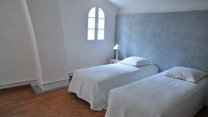 Una habitación con dos camas individuales, una mesita con lámpara, una ventana y suelo de madera.