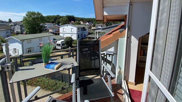 Un balcón con vistas a una zona residencial, un edificio blanco y una furgoneta estacionada.