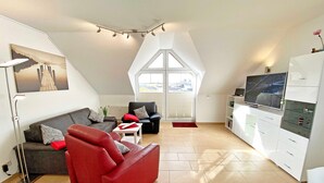 Una sala de estar moderna con un sofá rojo, un sillón negro y un mueble blanco con un televisor.