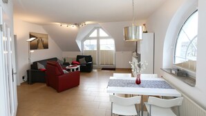 Una sala de estar moderna con comedor, que incluye un sofá rojo, un sofá negro y una mesa de comedor blanca con sillas.