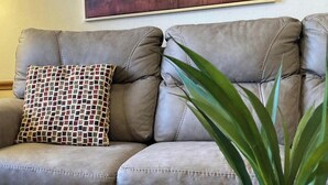 Ein graues Ledersofa mit einem gemusterten Kissen in einem Raum mit Stehlampe und Pflanze.