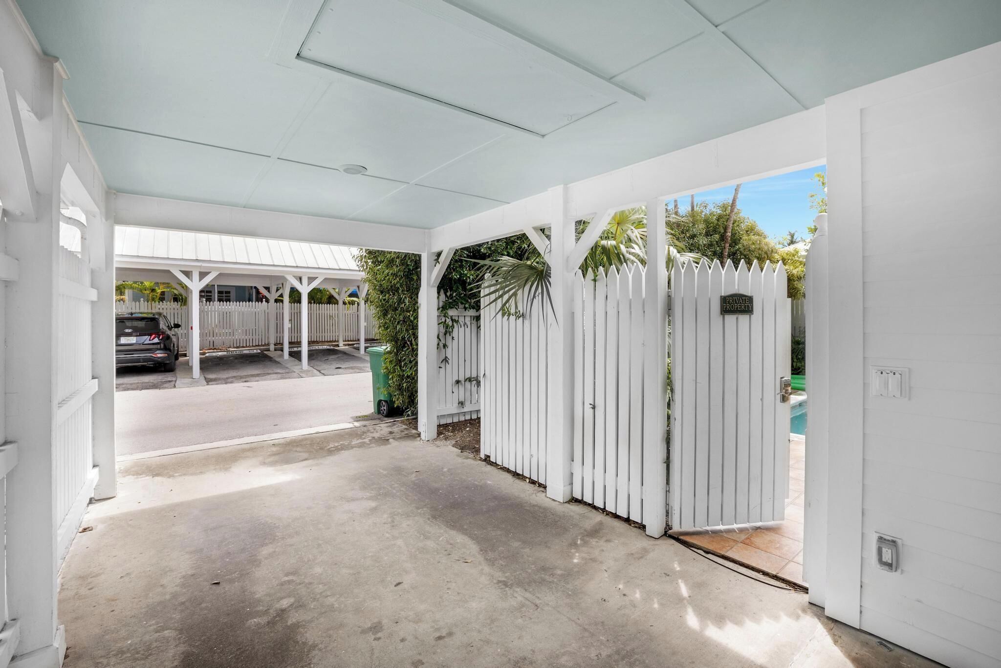 A covered parking area with a white fence, a gated entrance, and a visible car in the background.
