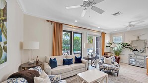 Un salon spacieux avec un canapé beige, des fauteuils à motifs, une table basse et un ventilateur de plafond.