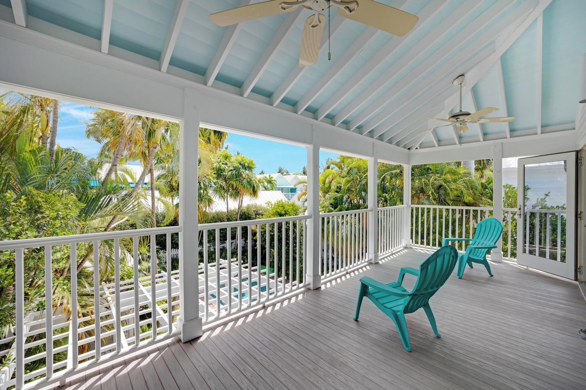 A covered outdoor area with white railings, two turquoise chairs, and a ceiling fan.