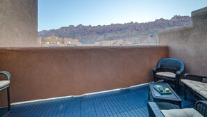 Een balkon met uitzicht op een bergachtig landschap, gemeubileerd met rieten stoelen en een kleine tafel.
