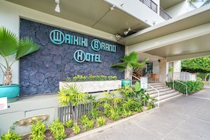Das Waikiki Grand Hotel mit Steinfassade, Außenbereich mit Sitzgelegenheiten und einem Schild, das eine Bar anzeigt.