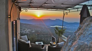 A terrace with wicker furniture, a TV, and a view of a sunset over mountains. - CORSE HOUSE EXCEPTIONAL SEA VIEW IN A VILLAGE BETWEEN SEA & MOUNTAINS (Speloncato)