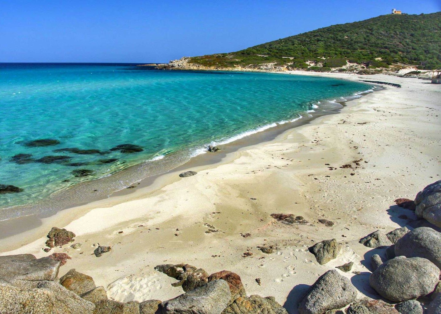 Una spiaggia con acque cristalline color turchese, una riva sabbiosa e affioramenti rocciosi.