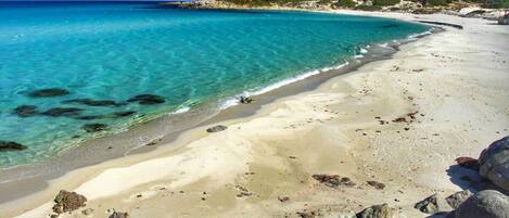 Una spiaggia con acque cristalline color turchese, una riva sabbiosa e affioramenti rocciosi.