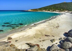 A beach with clear turquoise water, sandy shore, and rocky outcrops.