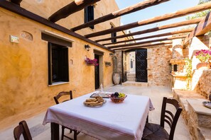 A cozy outdoor dining area with a table set for two, surrounded by stone walls and wooden beams.