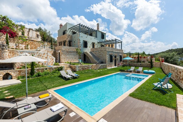 A pool area with lounge chairs, a stone building, and a clear blue sky.